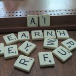Cream Scrabble tiles on a wooden table. The letters A and I are set up on the organizing piece while the other letters are scattered.