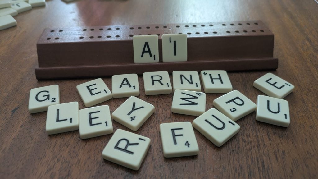 Cream Scrabble tiles on a wooden table. The letters A and I are set up on the organizing piece while the other letters are scattered.