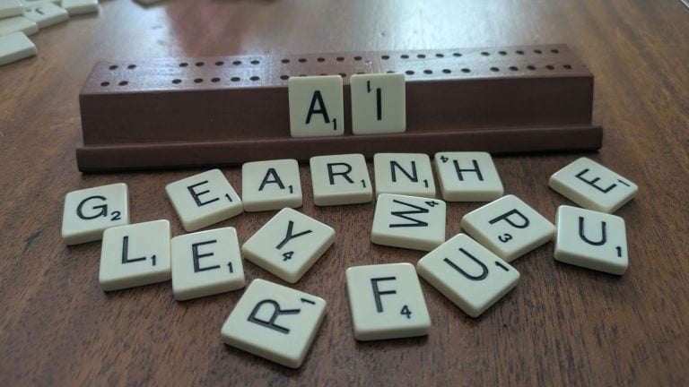 Cream Scrabble tiles on a wooden table. The letters A and I are set up on the organizing piece while the other letters are scattered.