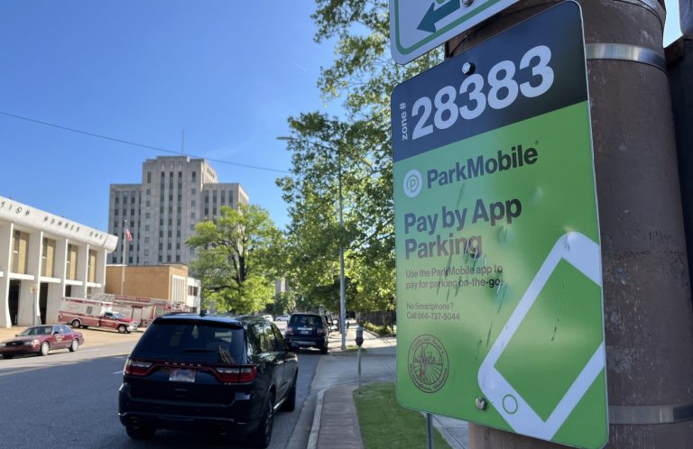Black hatchback car parked close to a ParkMobile App sign. Birmingham City Hall is in the distance center left, with a Birmingham Fire Department station slightly closer.